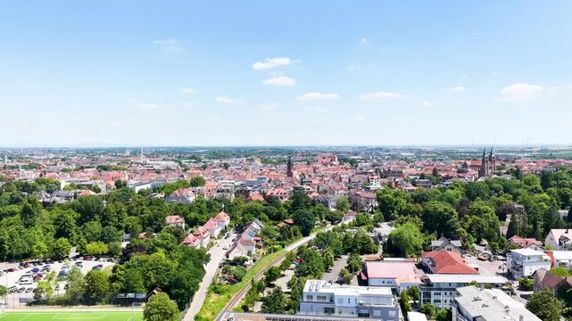 Spektakul&auml;re Weitwinkel-Luftaufnahme von Landau in der Pfalz unter blauem Sommerhimmel, die die dichte Altstadt, markante Kirchen und angrenzende gr&uuml;ne Parkanlagen zeigt.