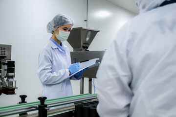 Naklejka premium Asian woman scientist in sterile uniform checking pharmaceutical product process on conveyor, concept of hygiene and quality assurance management.