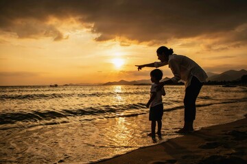 Fototapeta premium Silhouette of a mother pointing at the sunset for her young child on a beach