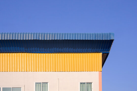 Modern industrial building with corrugated steel roof and metal sheet facade against blue clear sky. Minimalist architectural background 