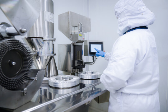 Pharmaceutical worker using medicine control digital panel in factory. Operating capsule filling machine via touchscreen in clean room. Pharmaceutical manufacturing with touchscreen interface.