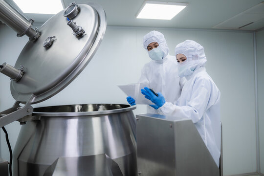 Two pharmaceutical factory workers in cleanroom suits checking production. Business and science concept in pharmaceutical industry. cleanroom manufacturing process, Medical quality control.
