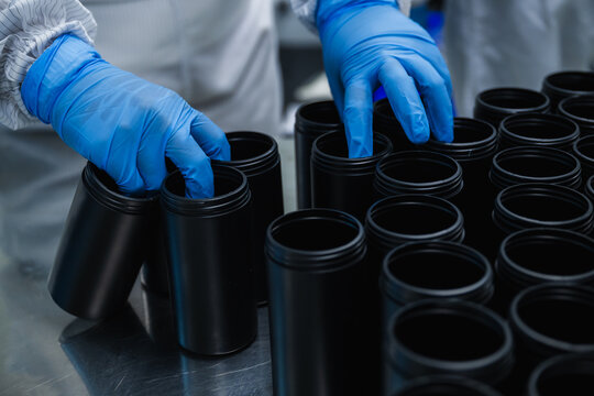 Close up of factory worker hands in blue gloves sorting black plastic bottles concept of pharmaceutical medicine packaging production line quality control