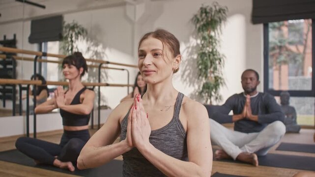 Group of people sitting in padmasana pose. Multicultural people sitting at mats and folding hands together. Multiethnic people doing lotus pose at yoga studio. People at yoga session.