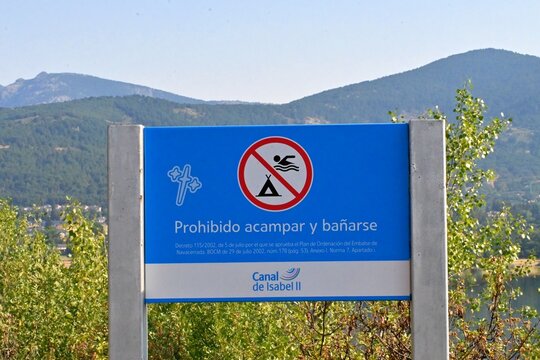 An information sign with the inscription Camping and swimming prohibited, placed near a mountain reservoir in Madrid, Spain.July 15, 2026