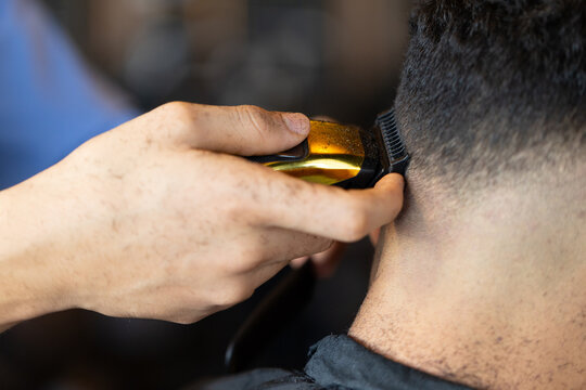African American barber trimming client's nape with clipper guard at barbershop on barber cape