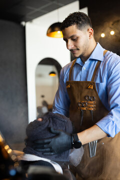 Barber and client with barber wrapping towel around client's head at barbershop wearing apron