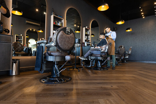 Vintage barber chair is sitting on polished wood floor at barbershop with pendant lights
