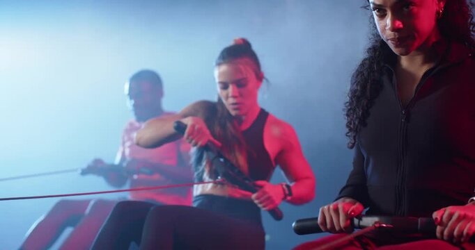 Diverse rowers after camera shift, female rower right pulling erg, wristwear pacing, copy space