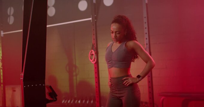 Adult African American woman breathing after set, checking smartwatch, adjusting stance at gym rig