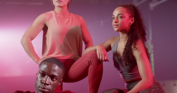 Diverse team in sportswear posing as camera panning under pink-purple lights, haze for shoot