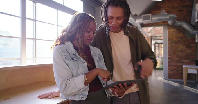 Co-workers collaborating over tablet at wooden counter tapping screen laughing walking up staircase