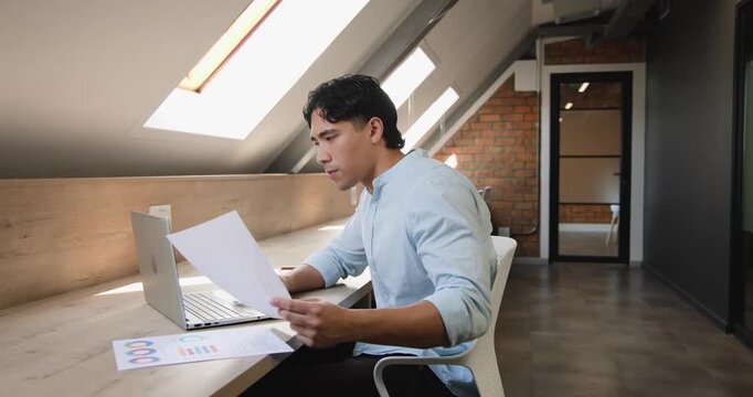 Man reading charts, typing on laptop and writing notes for report at skylit counter, copy space