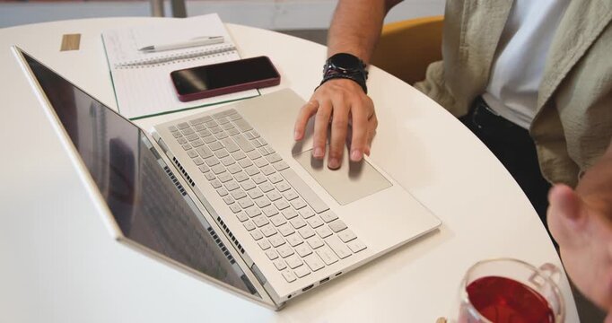 Man starting hands on laptop keys, typing, using trackpad, lifting mug working at round white table