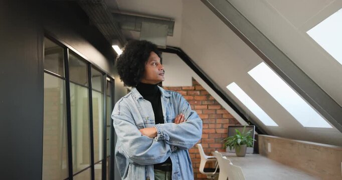 African American man in denim noticing loft skylight surveying desk uncrossing smiling to camera