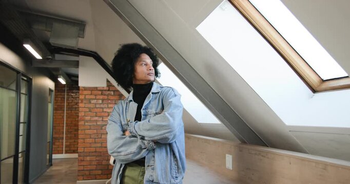 African-descent man leaning on ledge by skylights in jacket arms folded camera zooming making smile