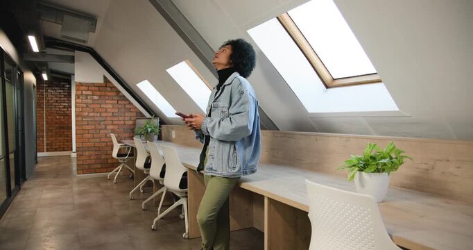 African-American man leaning by bench checking phone glancing skylight as camera moving, copy space