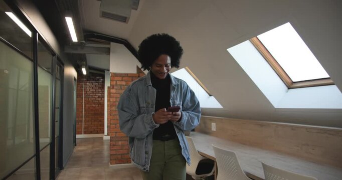 African man walking office corridor, checking red phone after ping, smiling in denim jacket