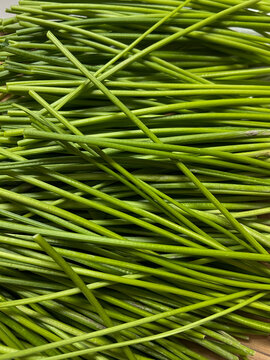 Top view abstract background of fresh vibrant green chives or garlic scapes stems stacked together
