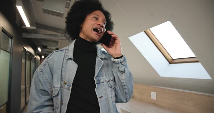 Receiving call, African American man walking in loft under skylights, reacting and talking on phone