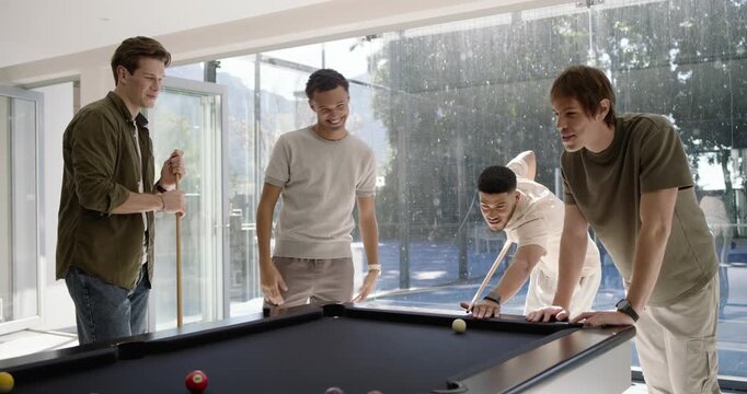 Diverse male friends playing pool at home, pointing to balls, lining up shots for fun