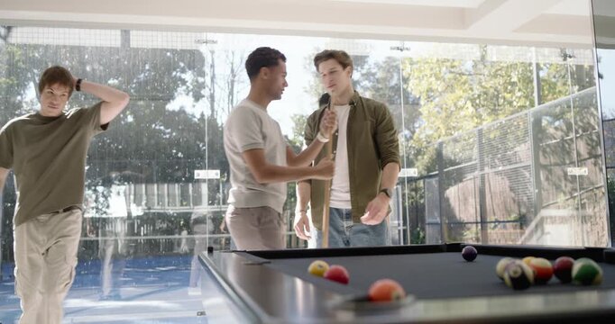 Four male pals gathering at pool table in glass room, exchanging fist bump, breaking, starting game