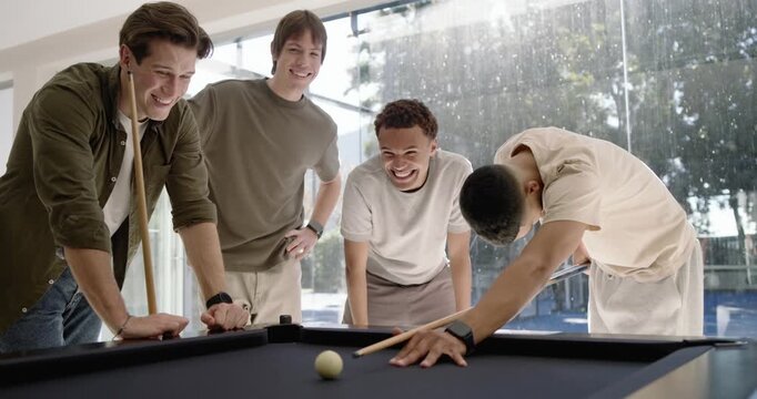 Diverse male friends watching shooter taking break shot to start game at pool table, racked balls