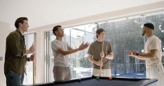 Diverse male friends playing pool by doors, cheering after shot, breaking rack, scattering balls