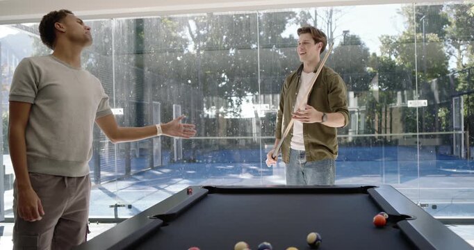 Diverse male friends breaking racked balls, exchanging cues and playing at black-felt pool table