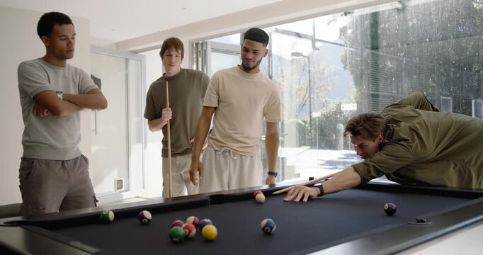 Diverse male pals at home pool table watching break shot scattering balls trading cues and chatting
