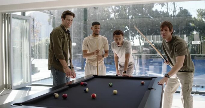 Four male friends starting game in rec room, rightmost lining and sinking balls on black-felt table