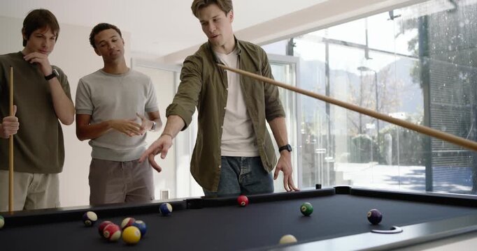 Men playing at pool table at home watching gesturing, shooter hitting cue ball, balls scattering