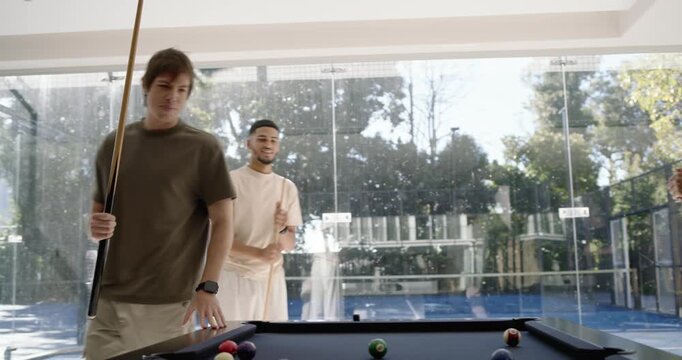 Diverse male friends inspecting black-felt table and balls in rec room breaking for casual game