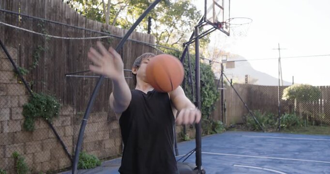 20s man bending, picking up orange basketball by portable hoop in backyard practicing finger spins