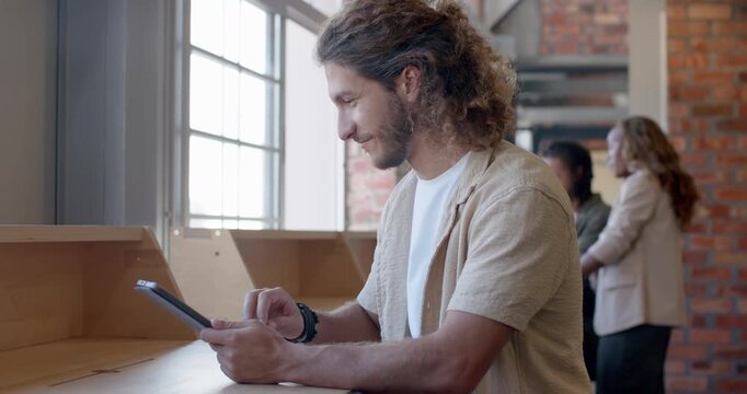 Diverse coworkers conversing in loft while man tapping tablet at counter, reviewing content