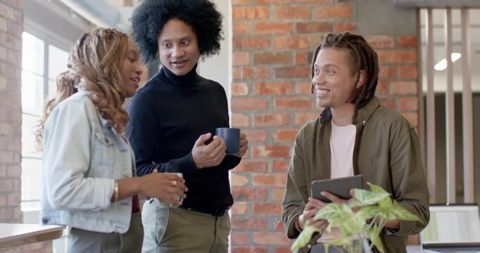 African American team laughing as woman explaining project by window with blue mugs, tablet
