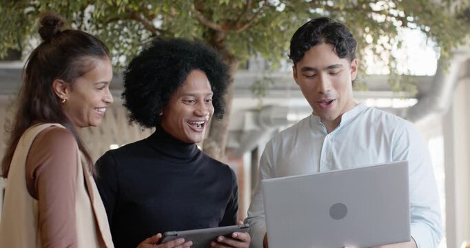Diverse team reacting to man holding laptop, reviewing slides on tablet, laughing under colonnade