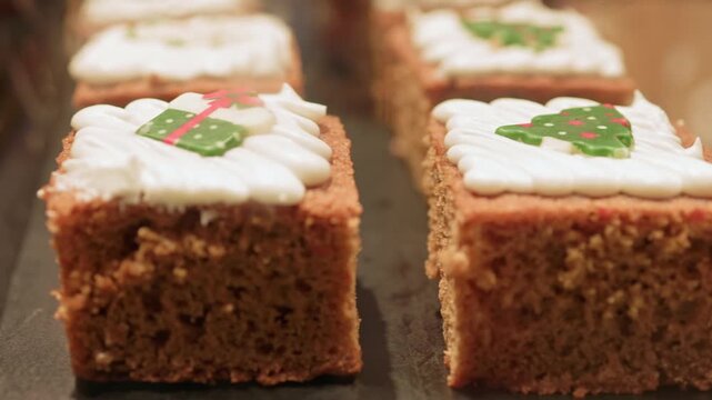 Delicious gingerbread cake squares with white frosting and festive holiday decorations, including christmas trees and gifts, are displayed on a tray in a bakery showcase for seasonal celebrations