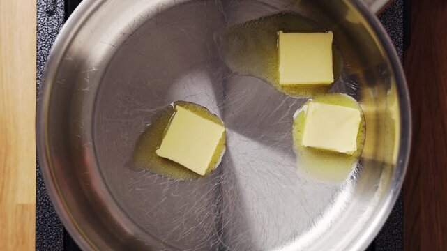 Butter pieces melt slowly in saucepan, starting rich sauce base. Chef melts butter carefully for smooth restaurant recipe. Melted butter brings flavor to fine dining kitchen cooking.