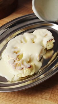 Hot creamy sauce pours slowly over baked cauliflower. Cooking healthy, nutritious cauliflower with rich creamy sauce. Vegetable dinner recipe comes together with warm creamy sauce.
