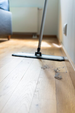 Flat mop approaching dust accumulation on a wooden floor in a bright home