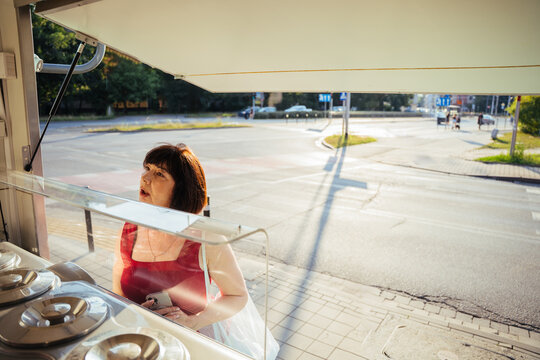 Curious mature woman choosing ice cream at street kiosk during sunny summer city walk