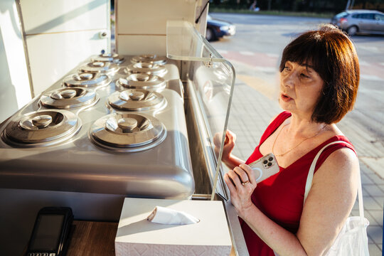 Thoughtful mature customer selecting gelato flavors at outdoor ice cream kiosk in summer