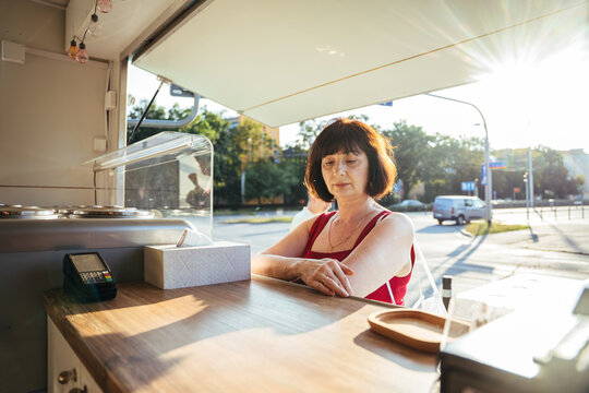 Thoughtful mature woman waiting at outdoor ice cream kiosk on sunny summer afternoon