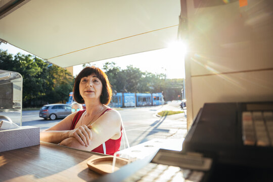 Relaxed mature woman waiting at ice cream kiosk counter on warm summer city evening
