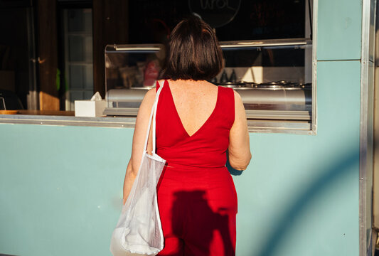 Elegant mature woman from behind ordering at street ice cream kiosk in warm evening light