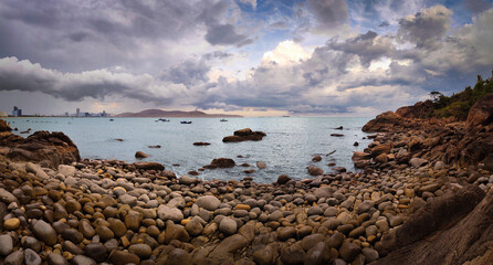 Panoramic view of Queens Beach (Bai Hoang Hau) in Ghenh Rang, Quy Nhon, Vietnam, with granite rocks, calm sea, cloudy sky, and the coastal city skyline © Olga Khoroshunova