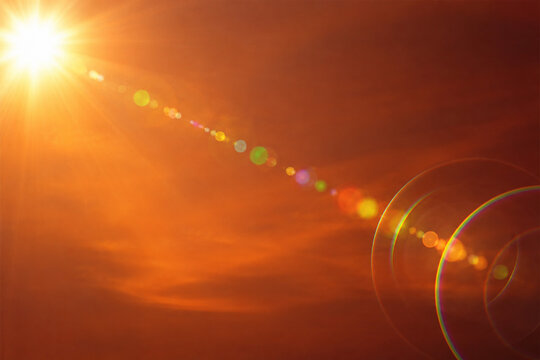 Golden sun flare with rainbow lens effects on bright orange sunset sky background for design.