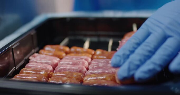 Hand in blue glove arranging raw marinated meat skewer in a black plastic tray at a food production facility
