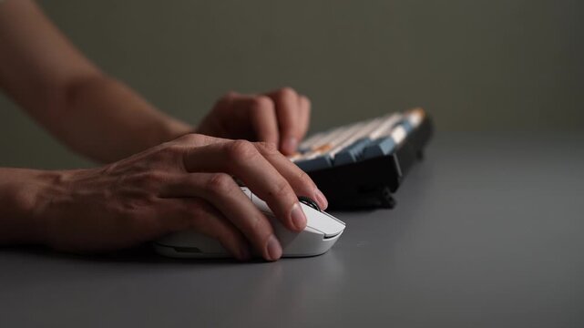 Side view of hands actively using wireless computer mouse and modern keyboard on grey desk, illustrating concepts of office work, gaming, digital creation, productivity, close-up, slow motion.